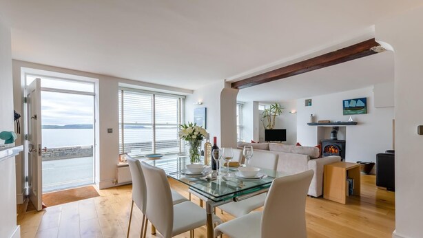 Una cocina moderna con una mesa de comedor de vidrio, sillas blancas, una estufa empotrada y vista al mar.