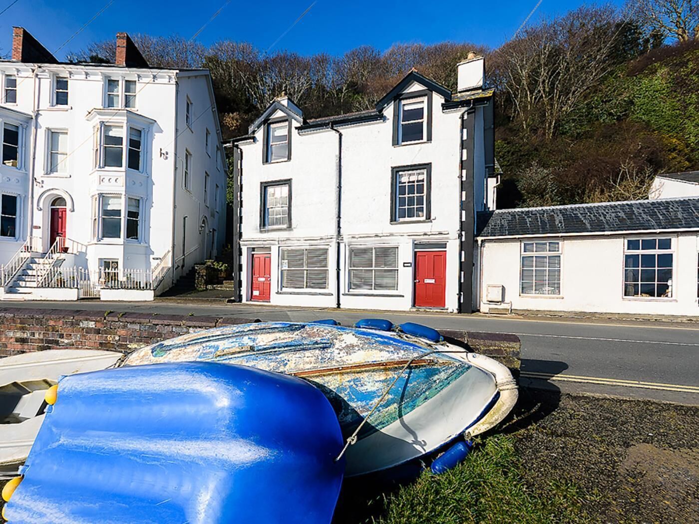 A coastal building with a red door and windows, a small boat on the grass, and a clear blue sky.