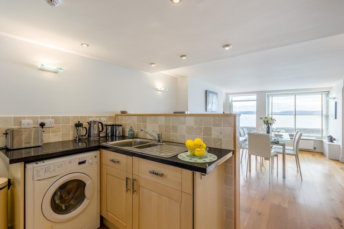 A modern kitchen with a washing machine, a sink, and a dining area with a view.