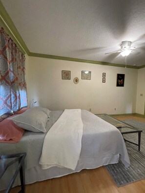 Ein Schlafzimmer mit einem Bett, einem Deckenventilator und einem Fenster mit Vorhängen.