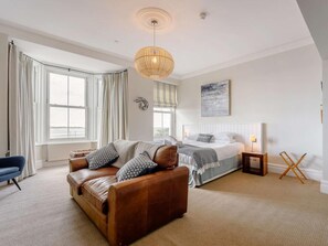 A bedroom with a bed, a brown leather sofa, a standing lamp, and a window with curtains. - 5 Bed in Aberdyfi (oc-dy026) (Aberdovey)