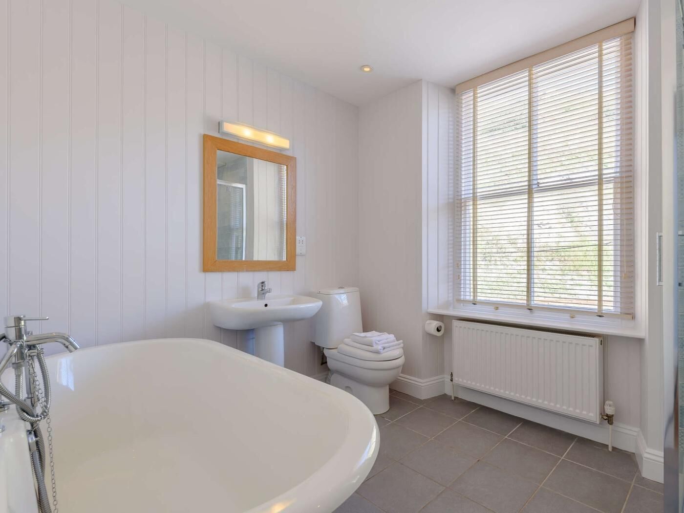 A bathroom with a bathtub, sink, toilet, and a window with blinds.