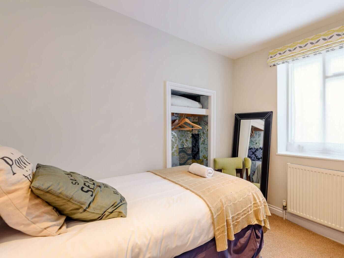 Een slaapkamer met een bed, kapstok, spiegel en radiator.