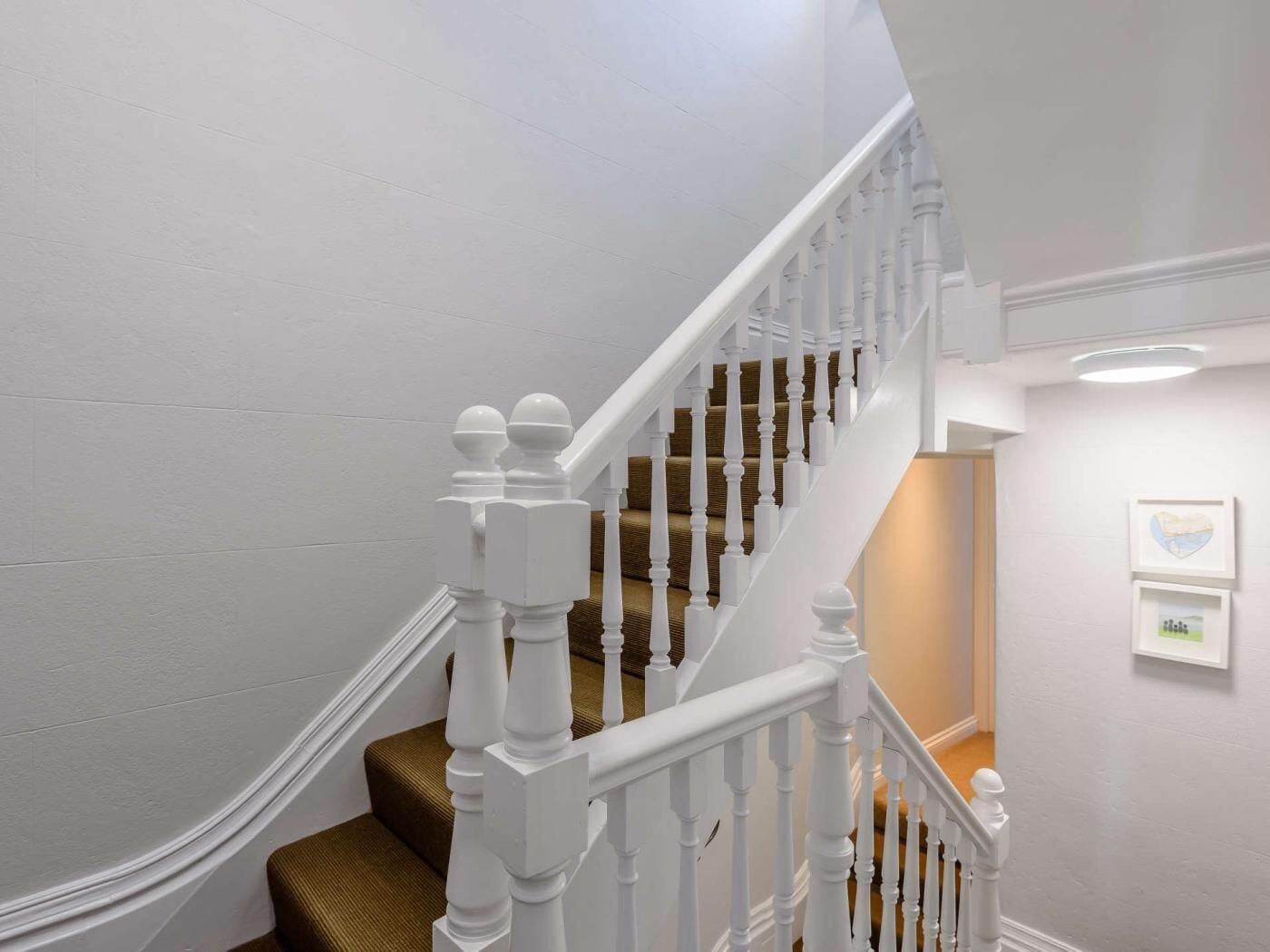 Een trap met witte balustrades en een landingsplaats met een bruin tapijt.