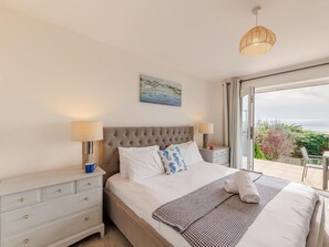 Quarto com cama, duas mesas de cabeceira, mesa de apoio, janela com vista e luminária pendente.