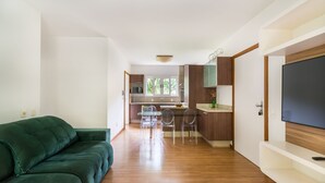 Uma sala de estar moderna com um sofá verde, uma cozinha com armários de madeira e uma televisão na parede da direita.