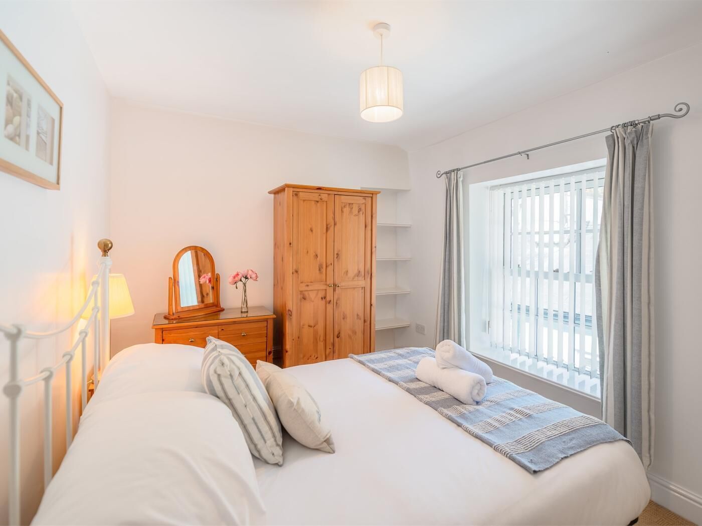 Une chambre à coucher avec un lit, une armoire en bois, un miroir, une lampe et une fenêtre avec des rideaux.