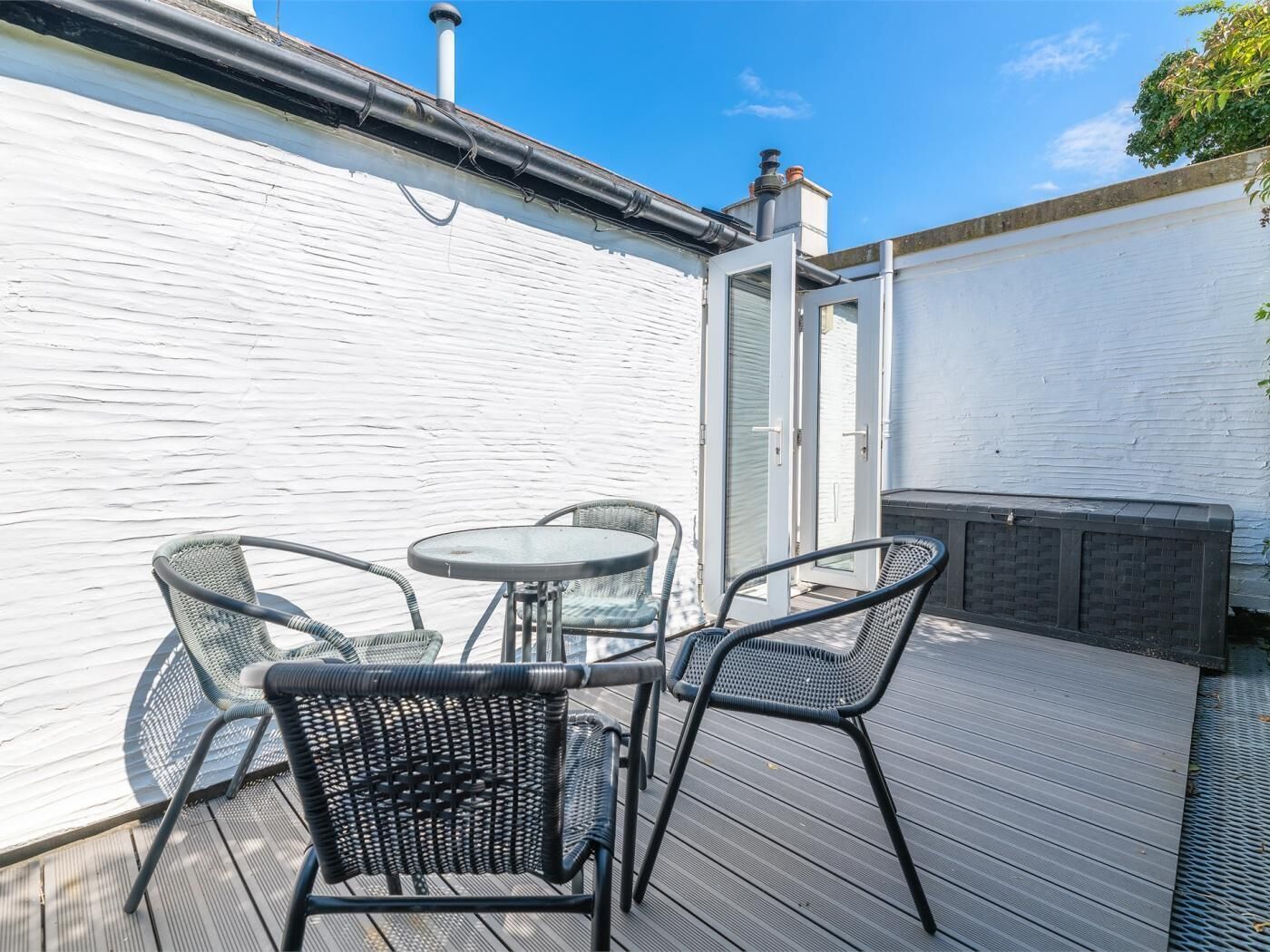 A deck with outdoor furniture, including chairs and a table, and a white wall with a door.