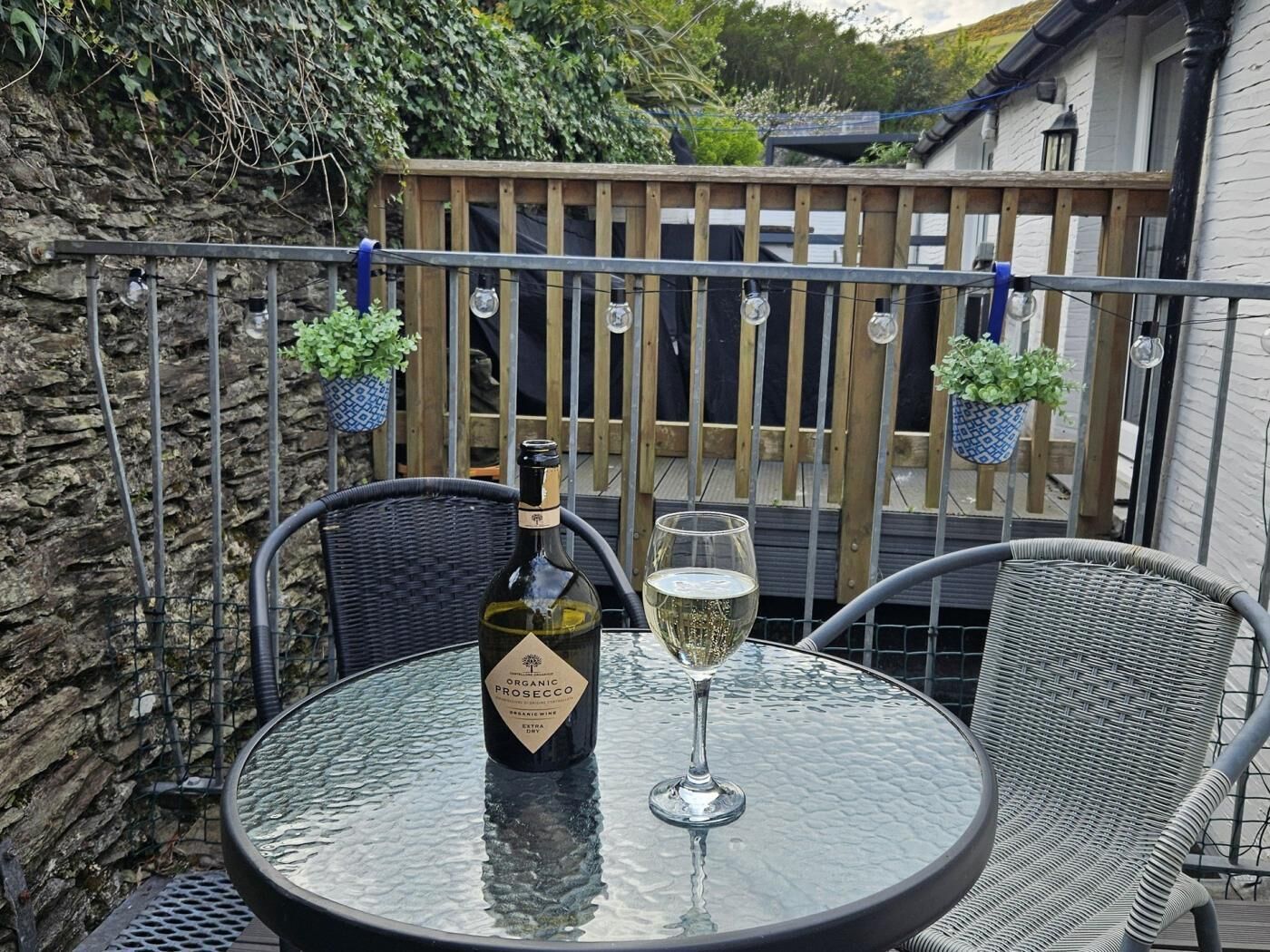 Uma mesa de vidro redonda com uma garrafa de prosecco orgânico e um copo de vinho numa varanda.