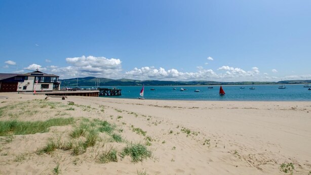 A beach with a building, a pier, and boats in the water. - 2 Bed in Aberdyfi (oc-dy047) (Aberdovey)