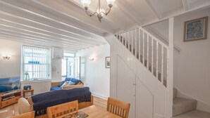 A dining area with a wooden table and chairs, a chandelier, a staircase, and a view of the outside. - 2 Bed in Aberdyfi (oc-dy047) (Aberdovey)