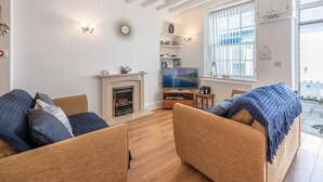 A modern living room with a fireplace, a television, and a large window with blinds. - 2 Bed in Aberdyfi (oc-dy047) (Aberdovey)
