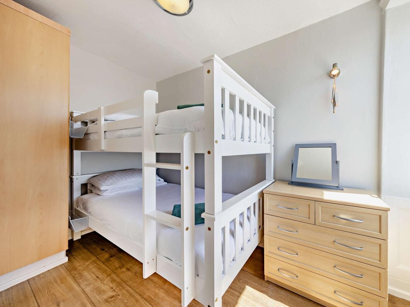 Un lit superposé avec un bureau et des tiroirs, un miroir et une armoire.