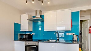 Eine moderne Küche mit weißen Schränken, einem schwarzen Backofen, einer Edelstahl-Dunstabzugshaube, einer Spüle und einem Wasserkocher.