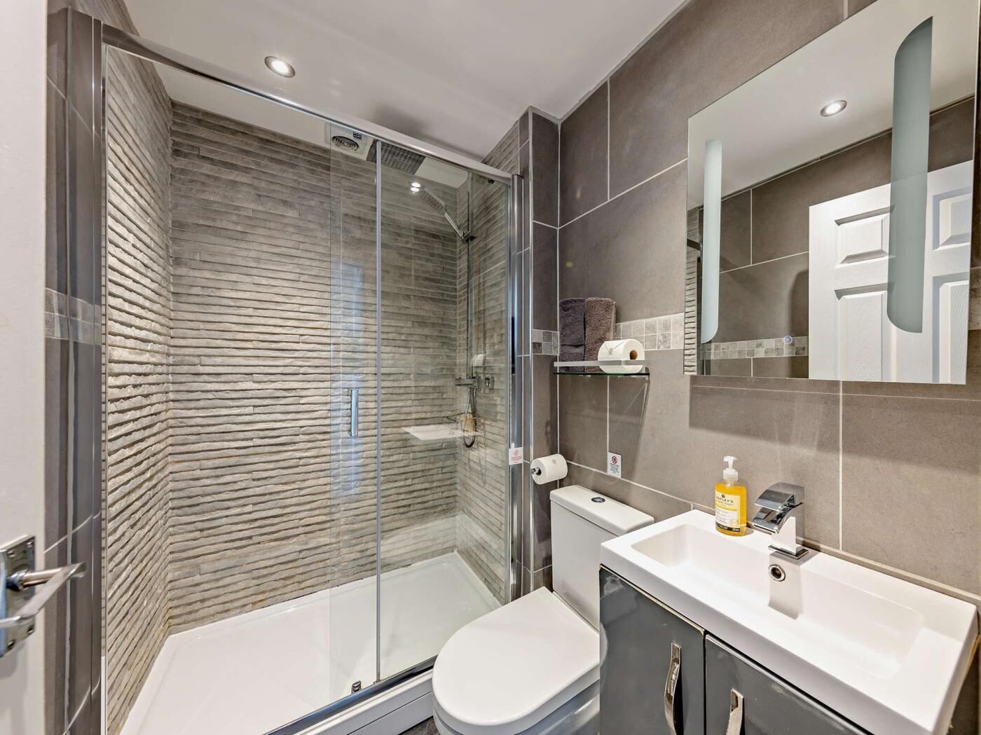 Un baño moderno con cabina de ducha de vidrio, inodoro blanco y tocador con espejo.