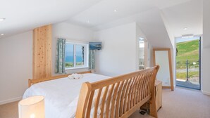 A bedroom with a bed, a TV, a window with curtains, and a view of the outdoors. - 2 Bed in Aberdyfi (oc-dy049) (Aberdovey)