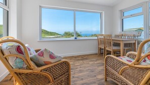 A room with a large window, wicker chairs, a wooden table, and a view of the sea. - 2 Bed in Aberdyfi (oc-dy049) (Aberdovey)