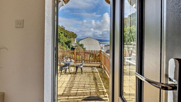 A balcony with a view of a wooden fence, a table with chairs, and a building in the background. - 3 Bed in Aberdyfi (oc-dy048) (Aberdovey)