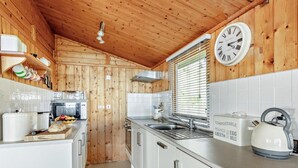 A compact kitchen with wooden walls, a white countertop, a kettle, and a clock. - 2 Bed in Aberdyfi (oc-dy050) (Aberdovey)