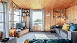 A cozy cabin interior with a wooden ceiling, a television on a wooden stand, a sofa, a bookshelf, and a view through a window. - 2 Bed in Aberdyfi (oc-dy050) (Aberdovey)