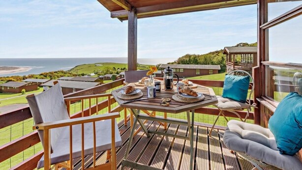 A wooden deck with a table set for breakfast overlooking a coastal landscape. - 2 Bed in Aberdyfi (oc-dy050) (Aberdovey)
