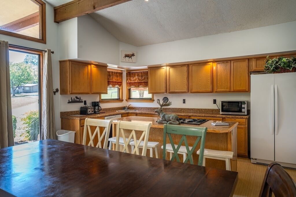 A kitchen with wooden cabinets, a dining table with chairs, a refrigerator, and a microwave.