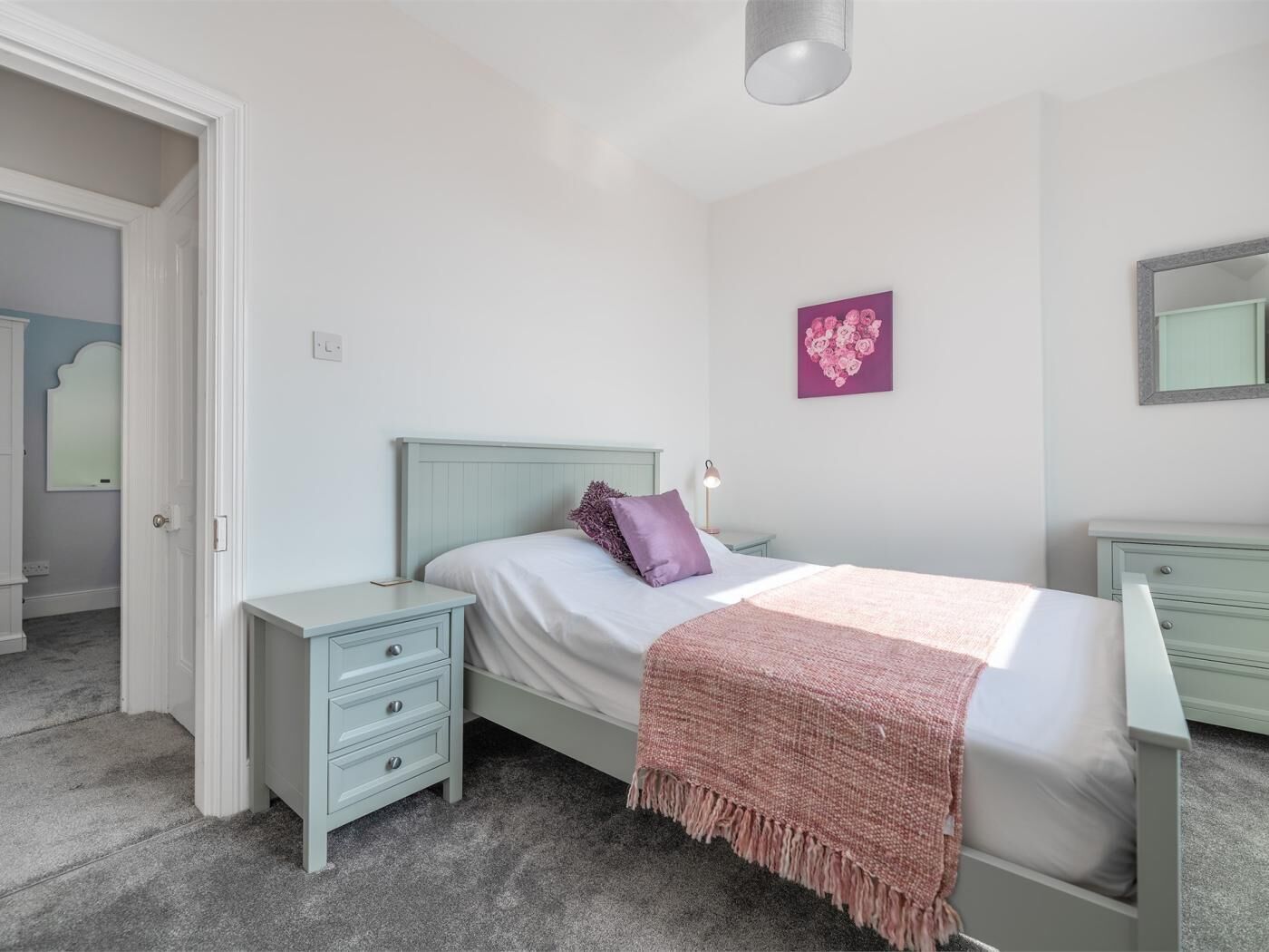 Une chambre à coucher comprenant un lit, une table de chevet, une commode, un miroir et un mur décoré d’un motif en forme de cœur.