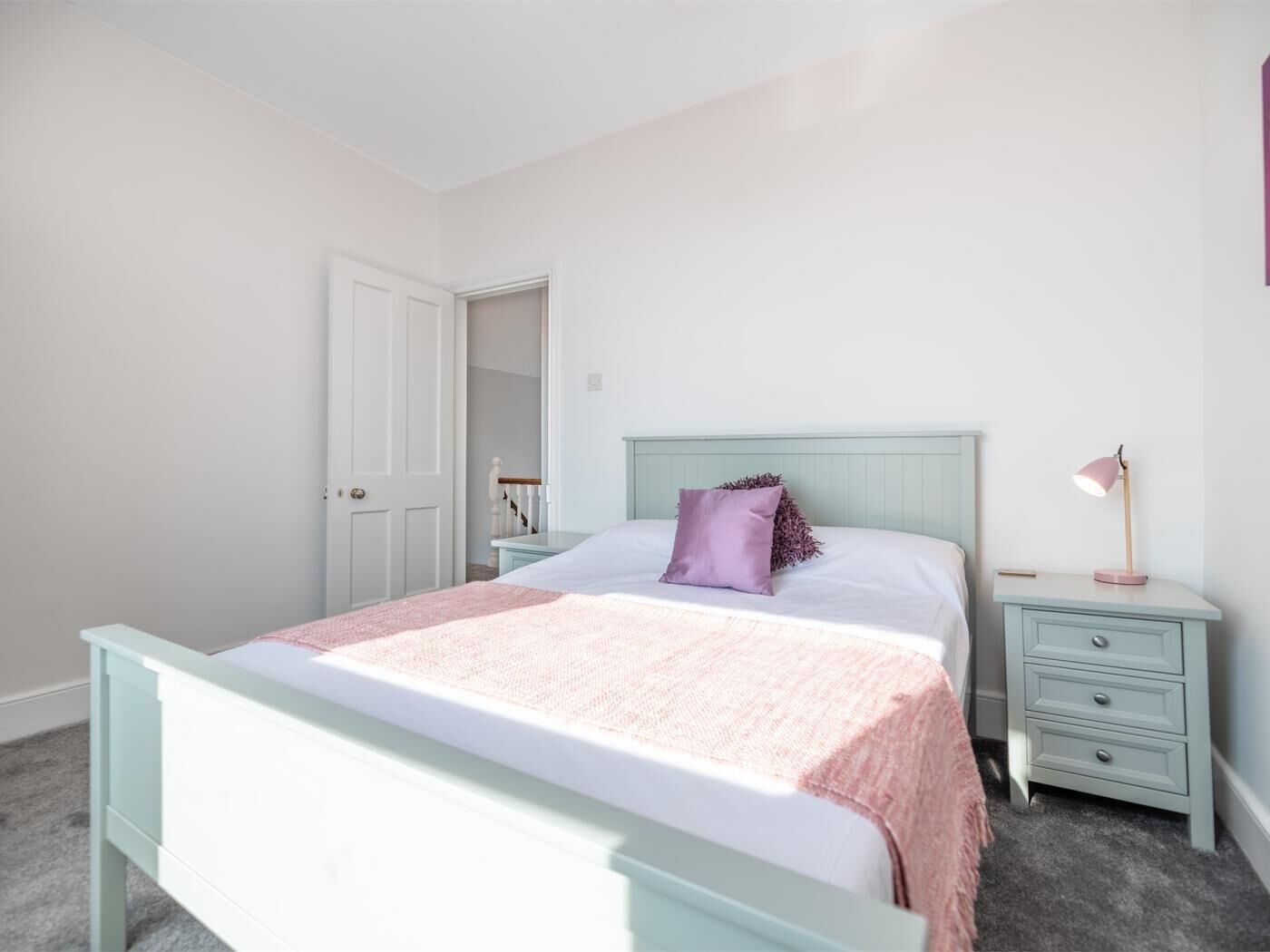 Ein Schlafzimmer mit einem Bett, Nachttischen, einer Wandlampe und einer Tür.