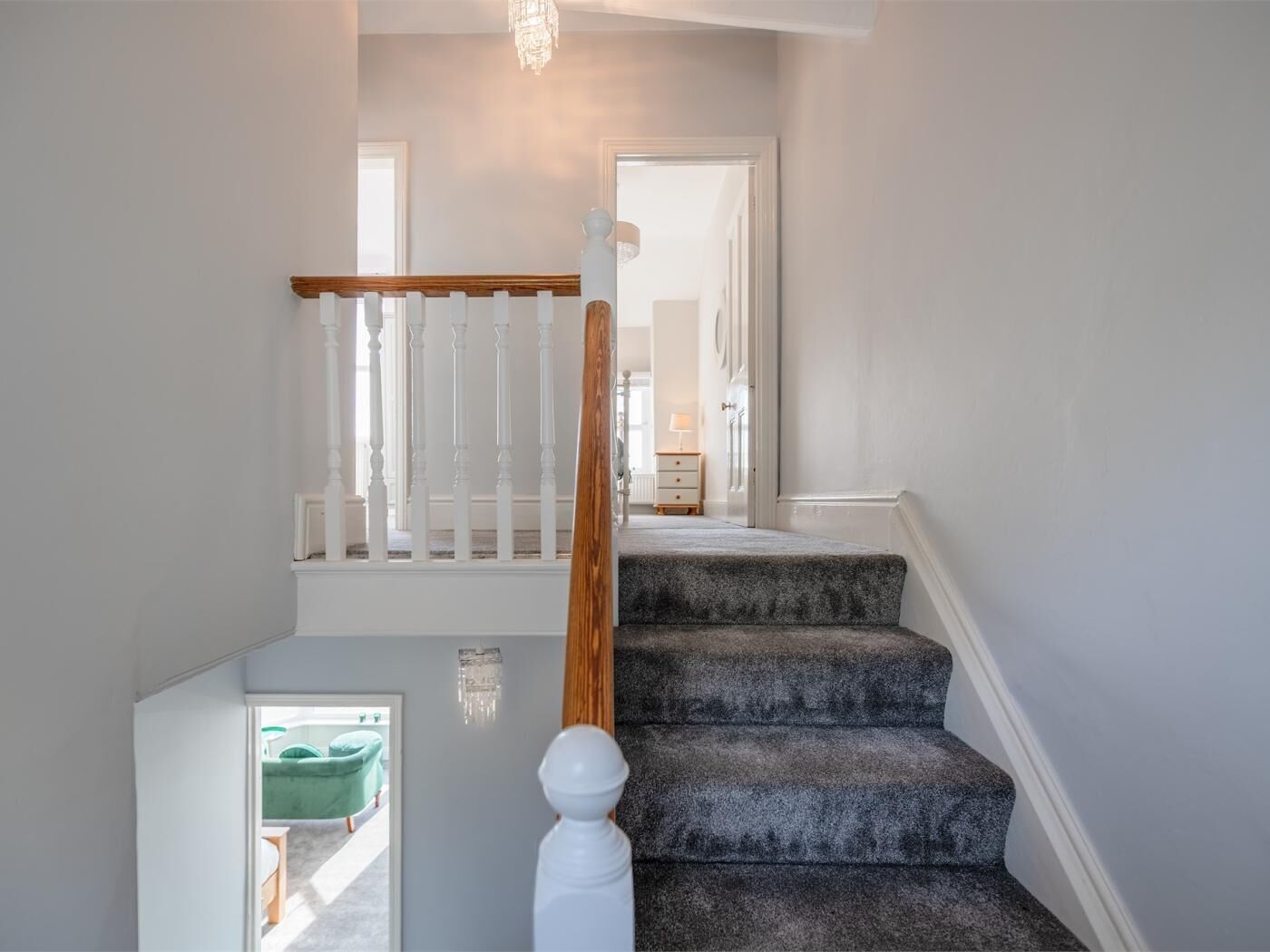 A staircase with a wooden handrail and a white balustrade, leading to a room with a bed and a nightstand.