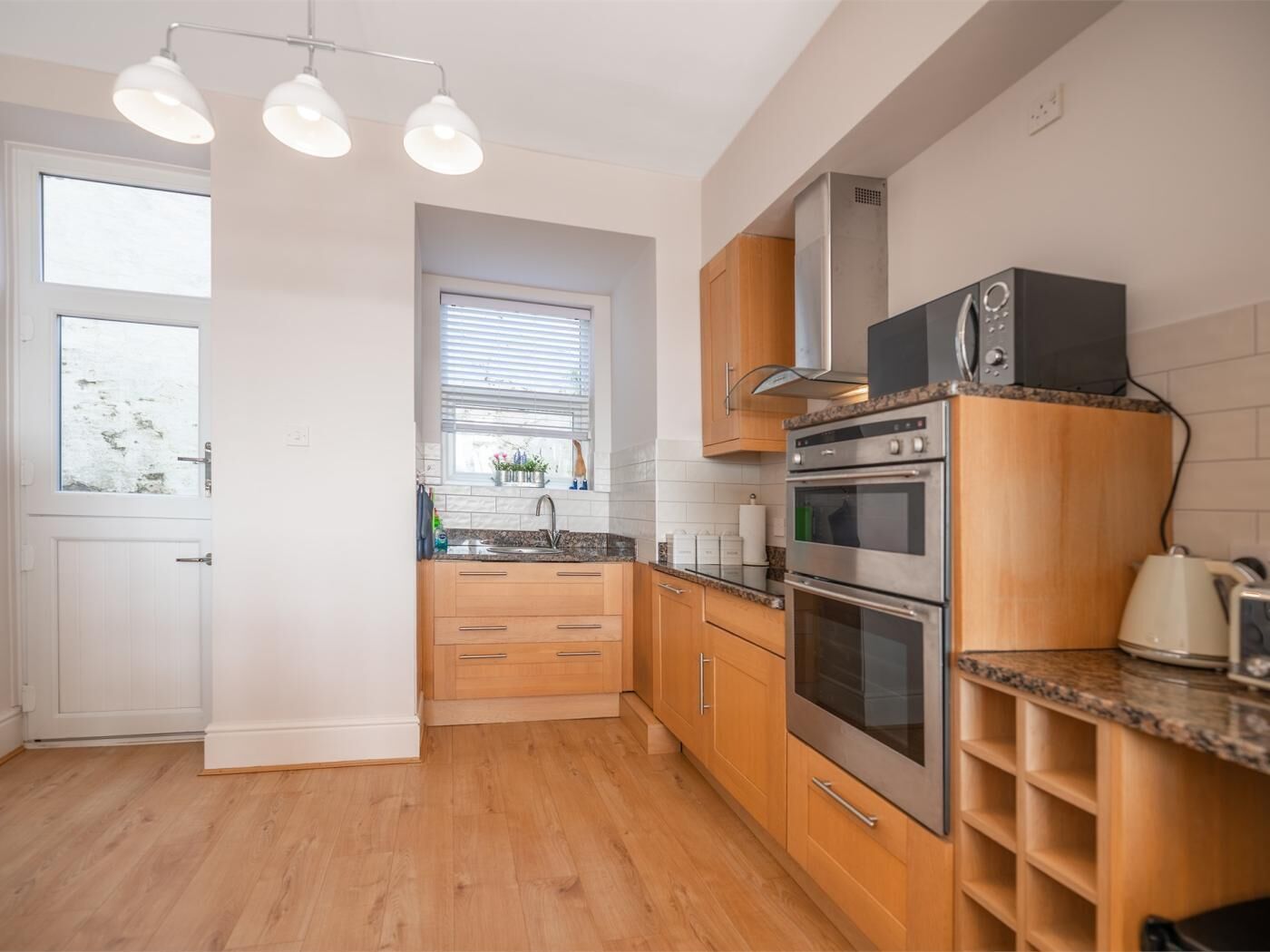 A modern kitchen with wooden cabinets, stainless steel appliances, and a window with blinds.