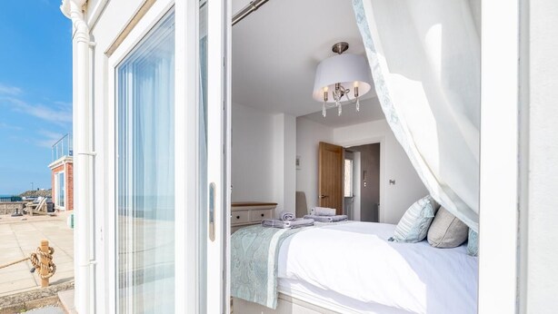 A bedroom with a large window, a bed with a canopy, a bedside table, and a nightstand. - 2 Bed in Tywyn (oc-dy052) (Tywyn)