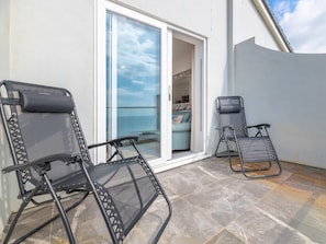 Ein Balkon mit zwei Liegestühlen, einer Glasschiebetür zu einem Innenraum und einer weißen Wand.