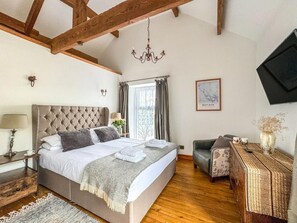 A bedroom with a large bed, a wooden ceiling, a chandelier, a desk, and a chair. - 3 Bed in Matlock (oc-86482) (Hackney)