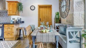 A rustic kitchen with wooden cabinets, a stone wall, and a dining area with a table set for two. - 3 Bed in Matlock (oc-86482) (Hackney)