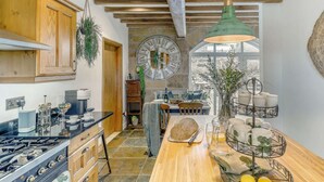 A kitchen with wooden cabinets, a stone wall, a large clock, and a hanging green pendant light. - 3 Bed in Matlock (oc-86482) (Hackney)