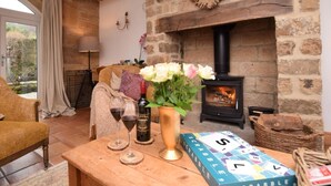 A cozy room with a stone fireplace, a wooden table with a Scrabble game, a vase of flowers, and a bottle of wine. - 3 Bed in Matlock (oc-86482) (Hackney)