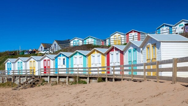 Una fila di casette colorate sulla spiaggia, con un recinto in legno in primo piano.