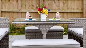 A glass-top table with wicker chairs, a white vase with flowers, and two drinks on plates. - 2 Bed in Umberleigh (oc-86611) (Cobbaton)