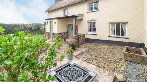 A two-story house with a thatched roof, stone foundation, and a paved courtyard. - 2 Bed in Umberleigh (oc-86611) (Cobbaton)