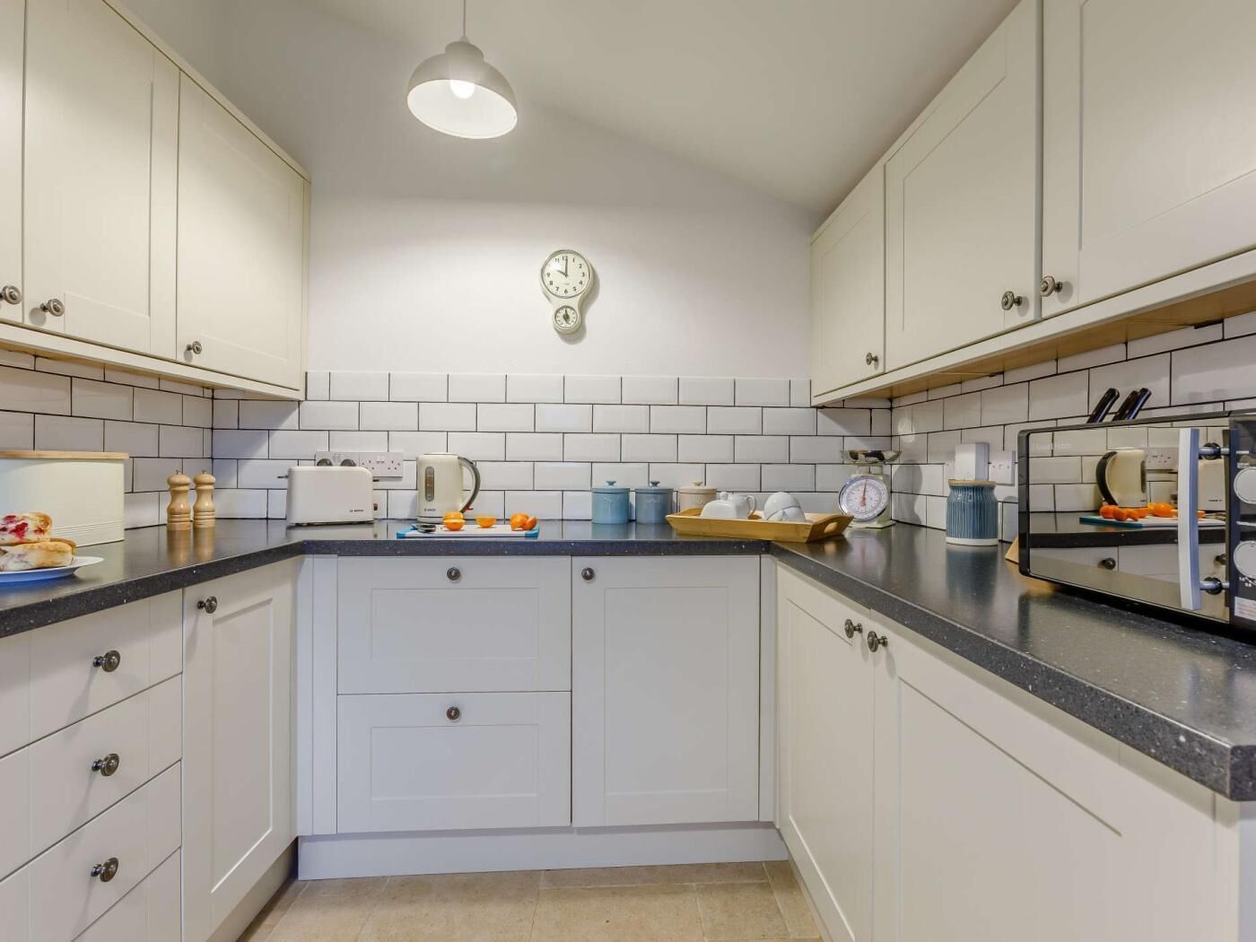 A kitchen with white cabinets, a black countertop, a clock on the wall, and a hanging light fixture.