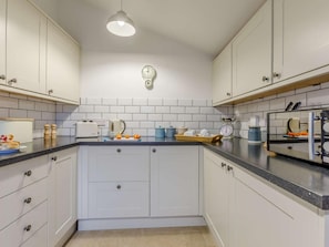 A kitchen with white cabinets, a black countertop, a clock on the wall, and a hanging light fixture. - 1 Bed in Bideford (oc-86571) (Hartland)