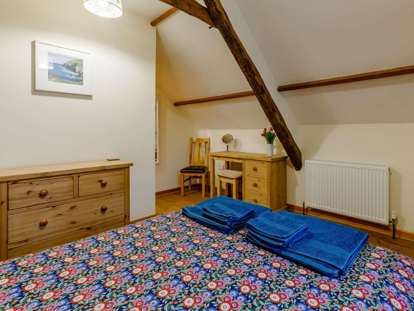 Ein Schlafzimmer mit einem Bett, einem Schminktisch, einem Schreibtisch, einem Stuhl, einer Heizung und einem gerahmten Bild an der Wand.