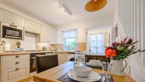A modern kitchen with white cabinets, a microwave, a stove, and a dining area with a table set for two. - 1 Bed in Keswick (oc-86560) (Keswick)