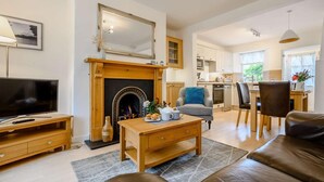 A living room with a fireplace, a television, a sofa, and a dining area with chairs and a table. - 1 Bed in Keswick (oc-86560) (Keswick)