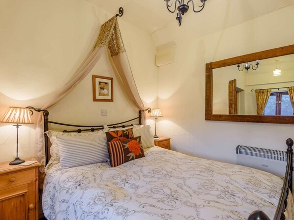 A bedroom with a canopy bed, bedside lamps, a mirror, and a radiator.