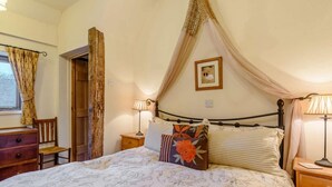 Um quarto com cama de dossel, uma cadeira de madeira, uma escrivaninha e um quadro na parede.