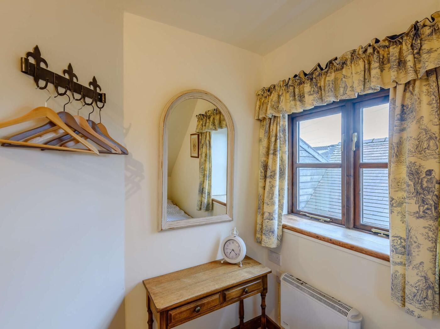 Une pièce avec un banc en bois, un miroir fixé au mur, un radiateur et une fenêtre ornée de rideaux à motifs.