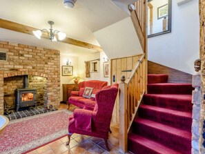 A cozy living room with a brick fireplace, a red sofa, a wooden staircase, and a tiled floor. - 2 Bed in Shrewsbury (oc-86590) (Leighton)