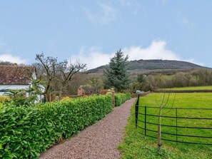 A rural pathway leading to a house with a red roof, surrounded by green hedges and a grassy field. - 2 Bed in Shrewsbury (oc-86590) (Leighton)