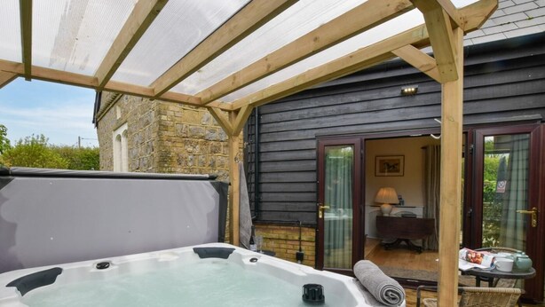 Una vasca idromassaggio sotto un gazebo in legno, un muro in pietra e una porta che dà su un ambiente con tavolo e sedie.